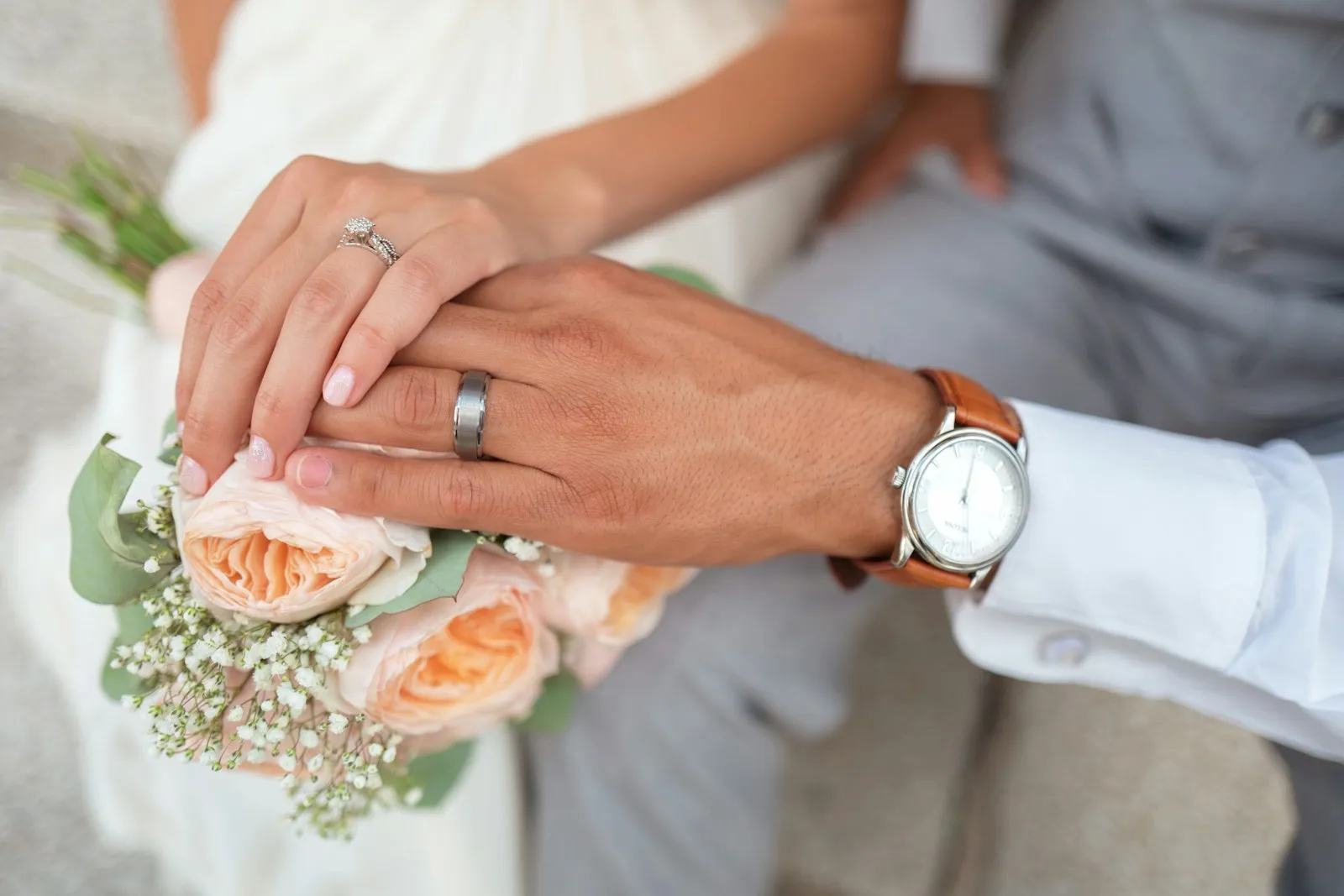 The couple’s hands holding the bouquet, rings on